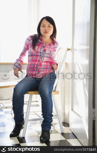 Pretty young Asian woman sitting on chair at table in kitchen.