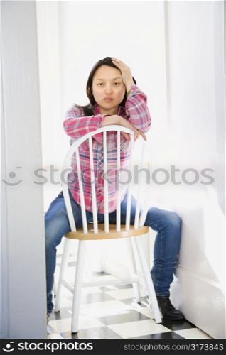 Pretty young Asian woman sitting on chair at table in kitchen.