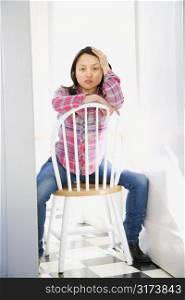 Pretty young Asian woman sitting on chair at table in kitchen.