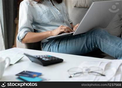 Pretty young Asian woman working with computer laptop to do home expenses and taxes in living room at home.