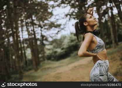 Pretty young attractive female runner listening to music and taking a break after jogging in a forest