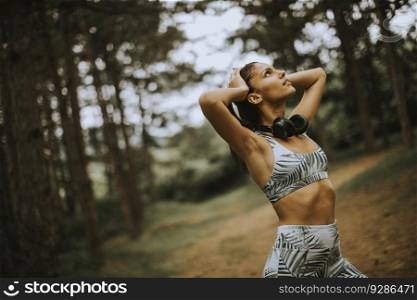Pretty young attractive female runner listening to music and taking a break after jogging in a forest