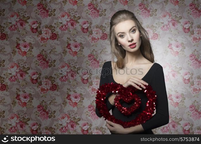 Pretty, young, attractive valentines girl with brown curly hair and brown make up is holding a heart.