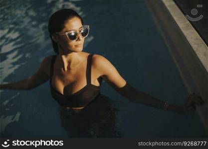 Pretty young attractive woman enjoys in the outdoor swimming pool in summer time