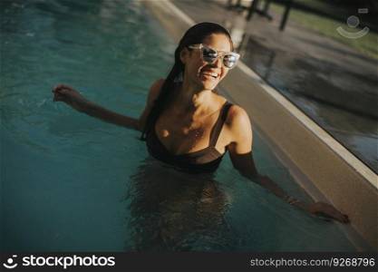 Pretty young attractive woman enjoys in the outdoor swimming pool in summer time