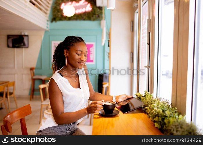 Pretty young black woman drinking coffee while looking at digital tablet in the cafe