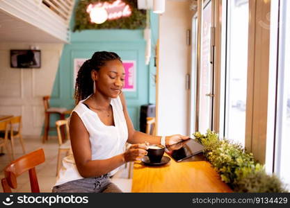 Pretty young black woman drinking coffee while looking at digital tablet in the cafe