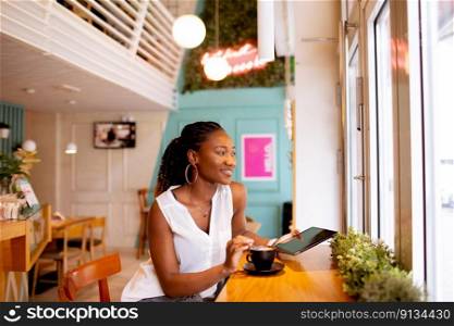 Pretty young black woman drinking coffee while looking at digital tablet in the cafe