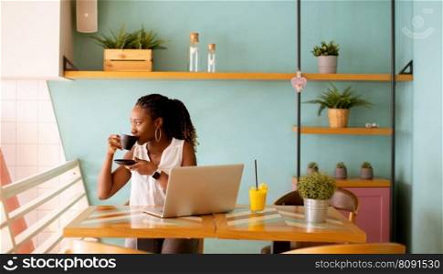 Pretty young black woman drinking coffee while working on laptop in the cafe