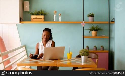 Pretty young black woman drinking coffee while working on laptop in the cafe