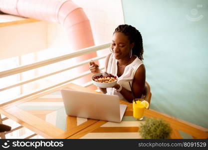 Pretty young black woman having a healthy breakfast while working on laptop in the cafe