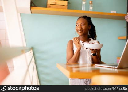 Pretty young black woman having a healthy breakfast while working on laptop in the cafe