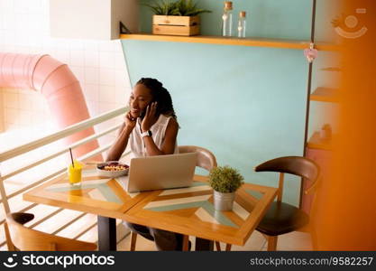 Pretty young black woman having a healthy breakfast while working on laptop in the cafe