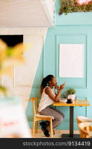 Pretty young black woman using mobile phone while having breakfast in the cafe