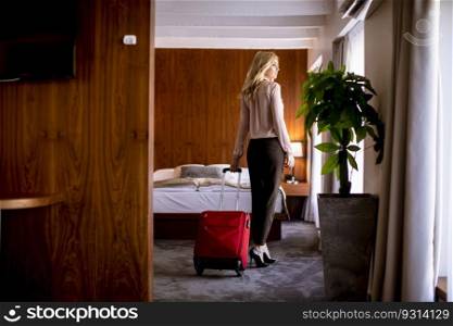 Pretty young blond businesswoman arrives in a hotel room with red suitcase