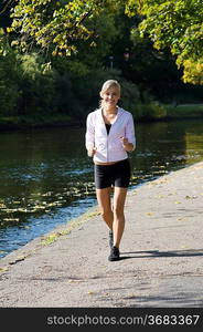 Pretty young blond girl running in the park near river