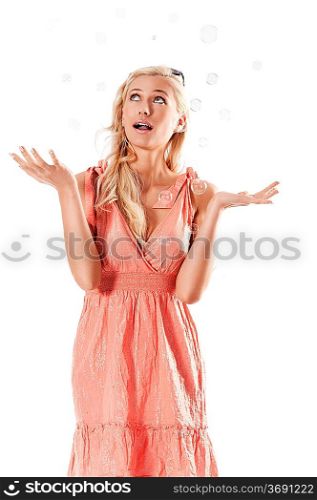 pretty young blond woman wearing a summer orange dress standing against white background looking towards the soap bubbles