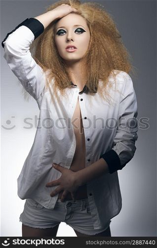 pretty young blonde girl with rock style dark make-up, voluminous hair-style, wearing sexy shirt on gray background