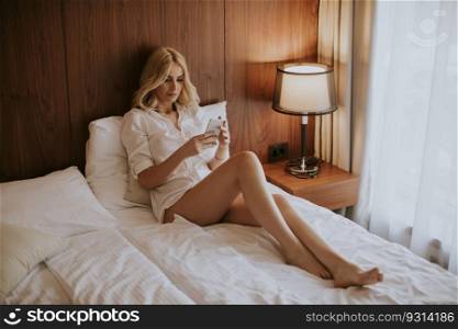 Pretty young blonde woman using mobile phone in the bed