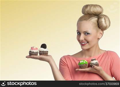 pretty young blonde woman with creative hair-style and colourful make-up showing variety of sweets cupcakes