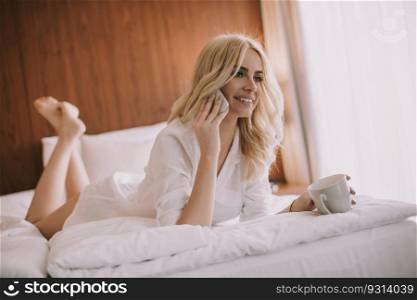 Pretty young blonde woman with mobile phone in the bed