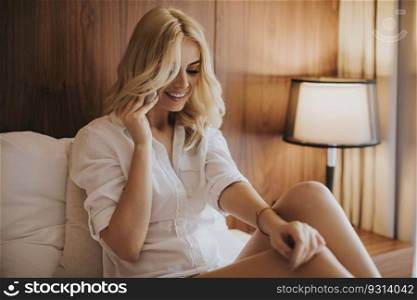 Pretty young blonde woman with mobile phone in the bed