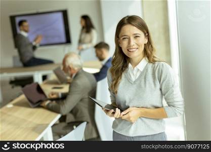 Pretty young busi≠ss woman at startup office with digital tab≤t in front of her col≤agues as team≤ader