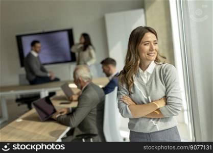 Pretty young business woman at startup office with arms crossed in front of her colleagues as team leader