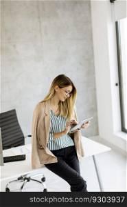 Pretty young business woman holding digital tablet and standing in the modern office