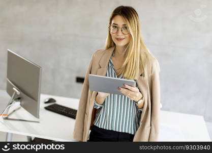 Pretty young business woman holding digital tablet and standing in the modern office