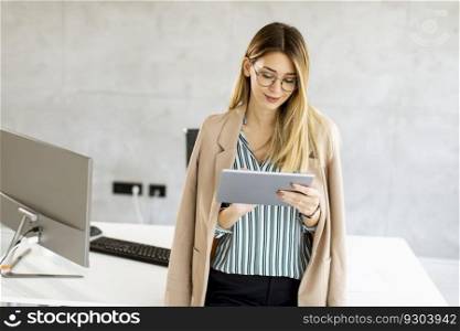 Pretty young business woman holding digital tablet and standing in the modern office