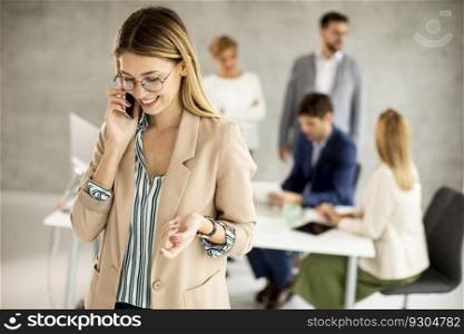 Pretty young business woman standing in the office and suing mobile phone in front of her team