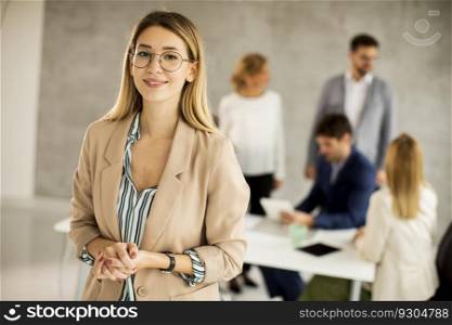 Pretty young business woman standing in the office in front of her team