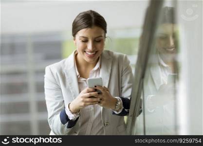 Pretty young business woman stands on the stairs at the modern office and use mobile phone