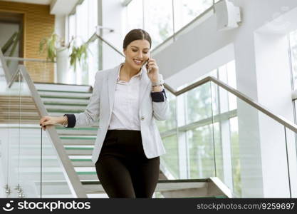 Pretty young business woman stands on the stairs at the office and use mobile phone