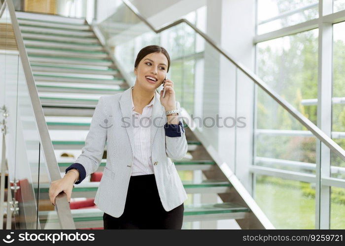 Pretty young business woman stands on the stairs at the office and use mobile phone