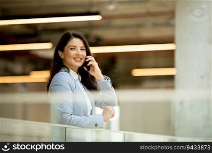 Pretty young business woman using mobile phone in the office hallway