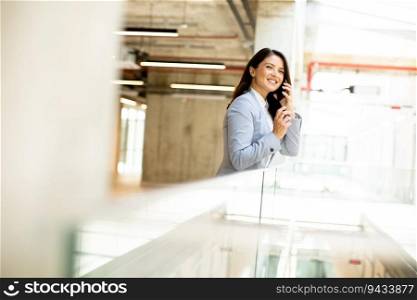 Pretty young business woman using mobile phone in the office hallway