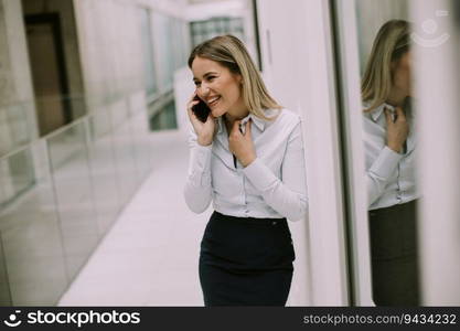 Pretty young business woman using mobile phone in the office hallway