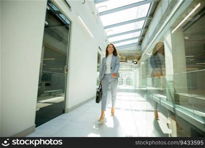 Pretty young business woman walking with briefcase in office hallway