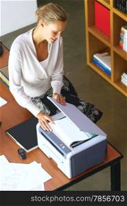 Pretty young businesswoman using copier machine at the office