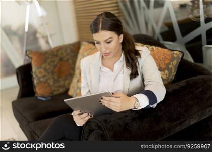 Pretty young businesswoman with digital tablet sitting in the sofa at office waiting room