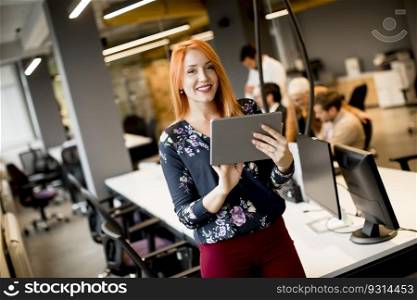 Pretty young businesswoman working on digital tablet while in the background team working in the modern office