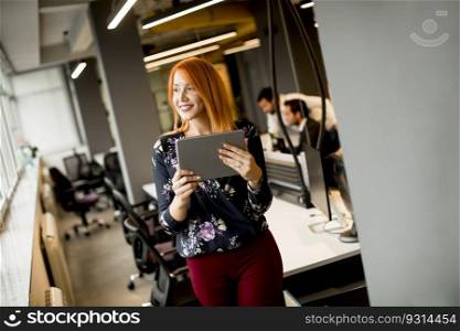 Pretty young businesswoman working on digital tablet while in the background team working in the modern office