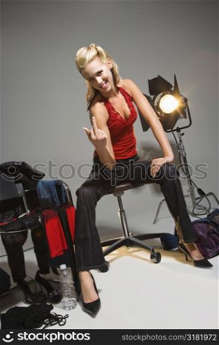 Pretty young Caucasian blonde woman sitting with studio lights giving middle finger.