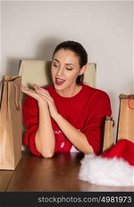 Pretty young Christmas woman sitting at office with shopping bags and laughing