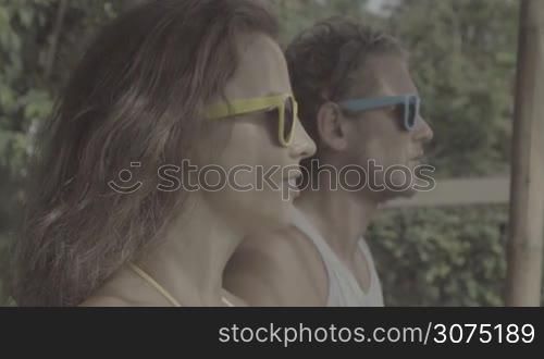 Pretty young couple sitting on the apartment&acute;s terrace during their holidays and enjoying beautiful view of the sea and mountains ahead of them in slow motion