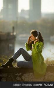 Pretty young curly hair woman listening music with smartphone by the river on a sunny autumn day