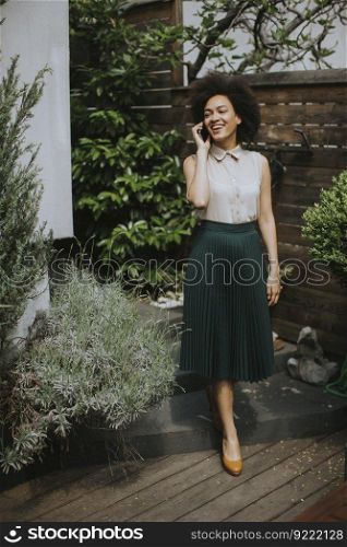 Pretty young curly hair woman with a mobile phone in his hand standing in the backyard