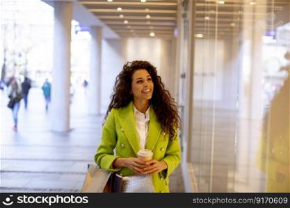 Pretty young curly hair woman with shopping bag and takeaway coffee cup in shopping